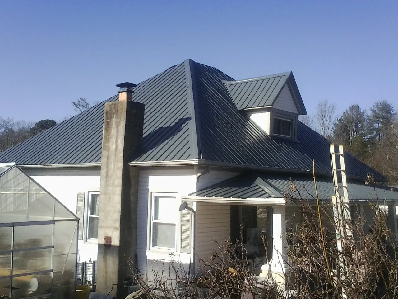 Dark blue standing seam metal roof on a white farmhouse with dormer — Slate & Tile Roof Repair by Roofing Brothers in Mayer