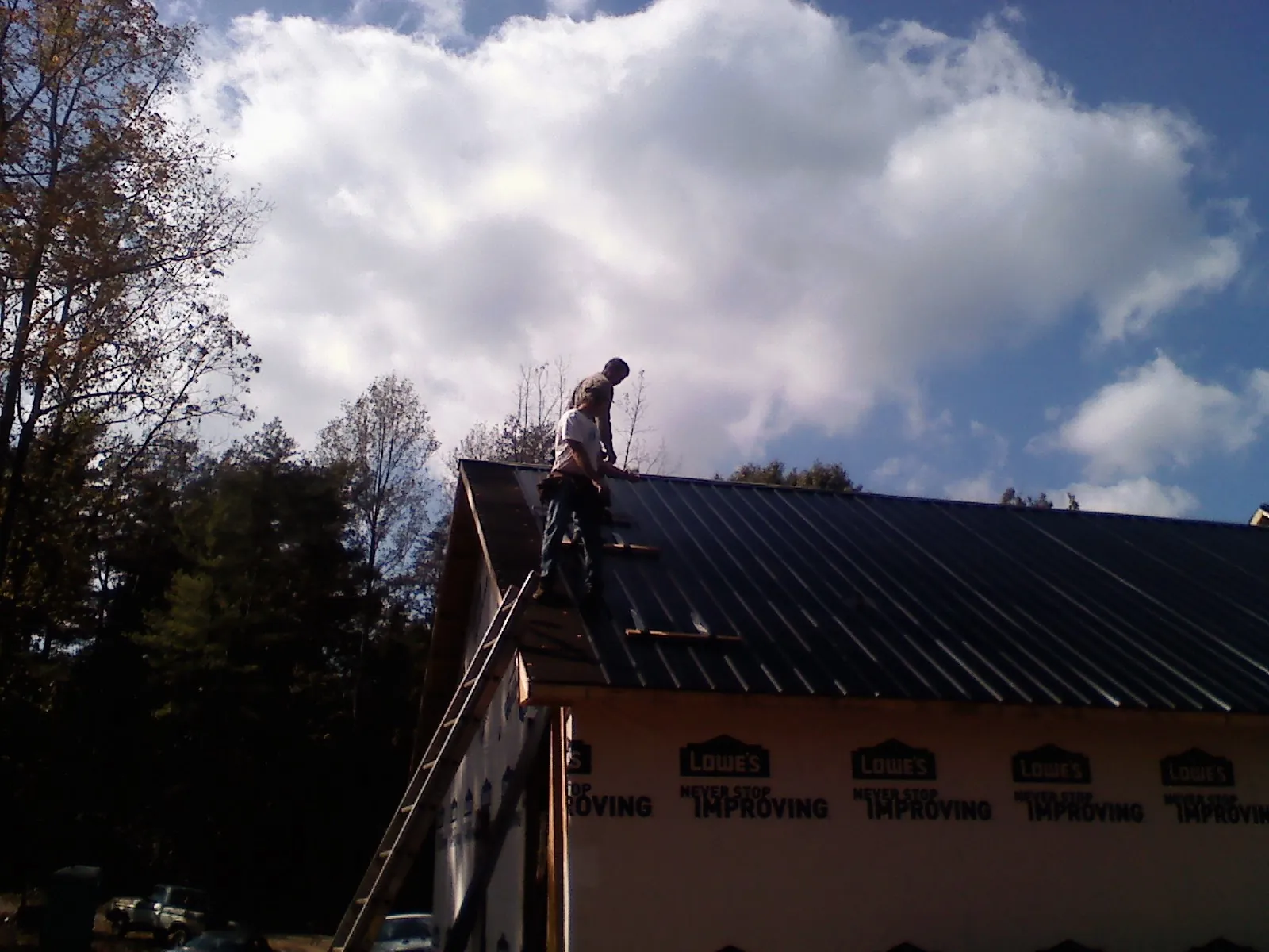 Roofer fastening dark metal panels high against a cloudy sky, from a Roof Inspection job in Mayer