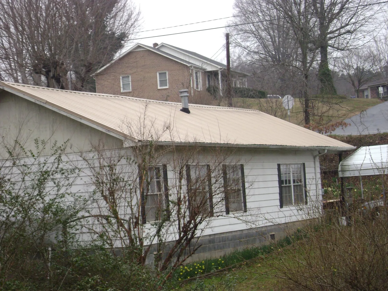 Tan metal roof on a white sided house set into a hillside — Commercial Roofing by Roofing Brothers in Mayer